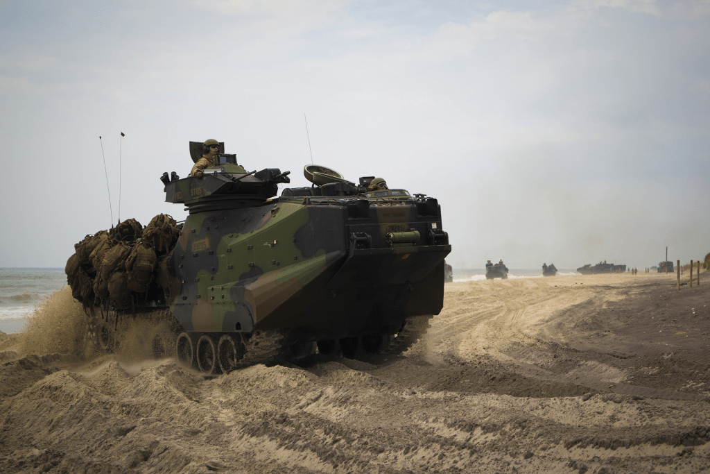 Das Bild zeigt einen amphibischen, gepanzerten Truppentransporter des Typs Assault Amphibious Vehicle AAV7 (auch genannt Amtrac) des US Marine Corps an einem Strand